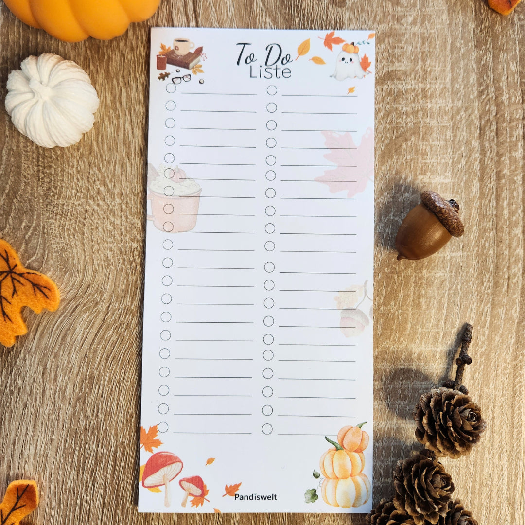 Herbstlicher To-Do-Listen Planerblock von Pandiswelt mit gemütlichen Illustrationen wie Kürbissen und Blättern, flach liegend auf Holz mit herbstlicher Natur-Deko wie Eicheln und Tannenzapfen